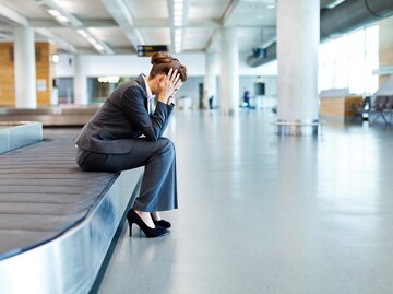 Frau sitzt auf Rollband am Flughafen und rauft sich die Haare. | © Getty Images/Neustockimages