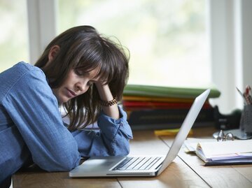 Frau sitzt mit aufgestütztem Kopf am Schreibtisch | © Getty Images/Ghislain & Marie David de Lossy