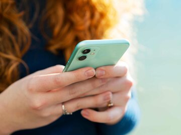 Frau mit roten Haaren hält Smartphone in der Hand - eine Nahaufnahme | © Getty Images/Tim Robberts