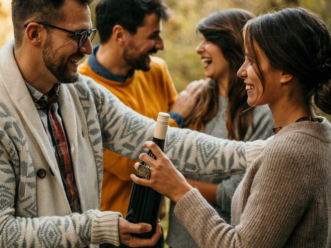 Frau und Mann begrüßen sich. Mann überreicht Frau einen Wein  | © Getty Images/MGM