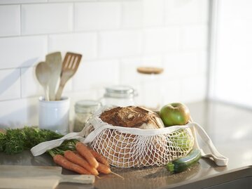 Einkaufsnetz mit Brot, Obst und Gemüse vor Glasbehältern und Holzlöffeln | © Getty Images/Dougal Waters