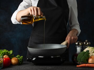 Frau in Kochschürze gießt Öl in Pfanne | © AdobeStock/Anton