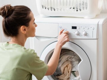 Junge Frau benutzt Waschmaschine | © Adobe Stock/LIGHTFIELD STUDIOS