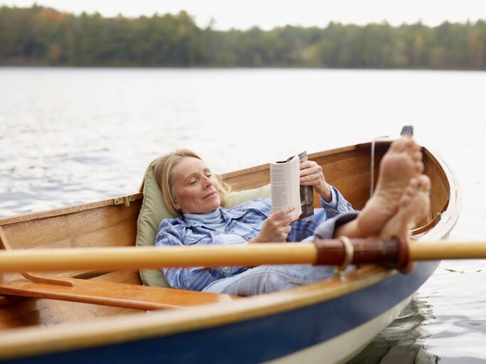 Eine Frau liegt gemütlich in einem Ruderboot und liest  | © GettyImages / Dann Tardif