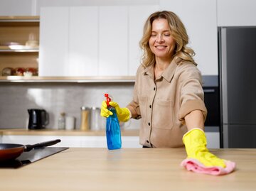Eine Frau putzt einen Küchentisch mit einem blauen Reinigungsmittel  | © Getty Images / Andrii Borodai
