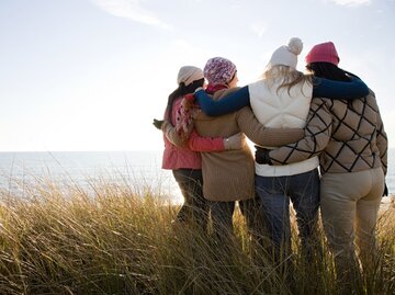 Eine Gruppe von vier Frauen steht in der Natur und hält sich in den Armen | © Getty Images / Image Source