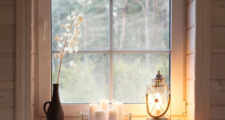Laterne, Kerzen und Vase mit Trockenblume auf Fensterbrett | © AdobeStock/Olga Ionina