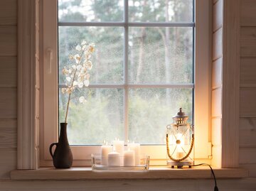 Laterne, Kerzen und Vase mit Trockenblume auf Fensterbrett | © AdobeStock/Olga Ionina