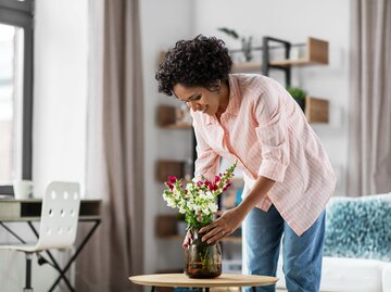 Frau stellt Vase mit Blumen auf den Tisch | © AdobeStock/Syda Productions