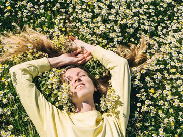 Eine Frau liegt in einer Blumenwiese im hohen Grass. | © Getty Images / Tatiana Maksimova