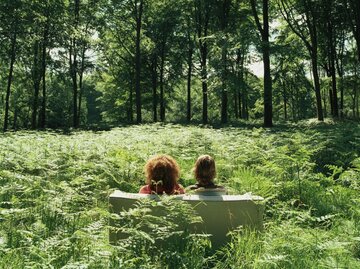 Zwei Frauen sitzen auf einer grünen Couch mitten im Wald. | © Getty Images / Martin Barraud