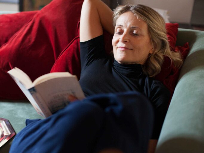 Frau liegt auf der Couch und liest ein Buch | © Getty Images/Kathrin Ziegler