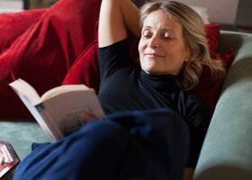 Frau liegt auf der Couch und liest ein Buch