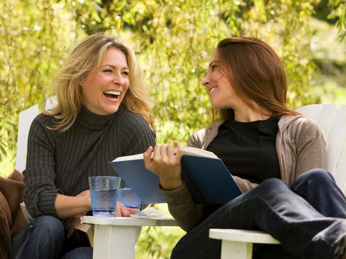 Zwei Freundinnen lachen und halten ein Buch in der Hand  | © Getty Images/Kevin R. Morris