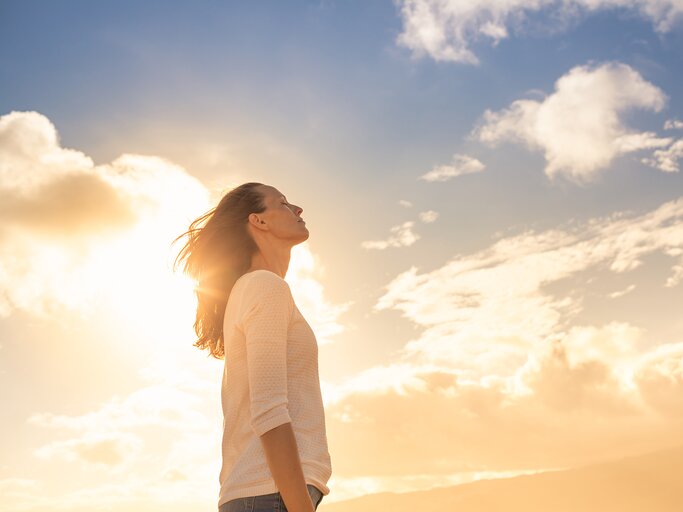 Eine Frau steht vor strahlendem Sonnenschein und blauem Himmel | © GettyImages/kieferpix