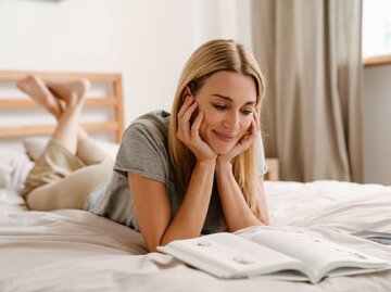 Frau liest Buch auf dem Bett liegend | © Adobe Stock/Drobot Dean