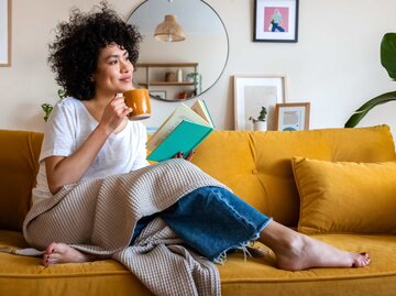 Frau sitzt auf dem Sofa und liest ein Buch. | © Adobe Stock/Daniel