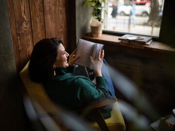 Eine Frau sitzt am Fenster und liest | © Getty images / Anastasiia Krivenok