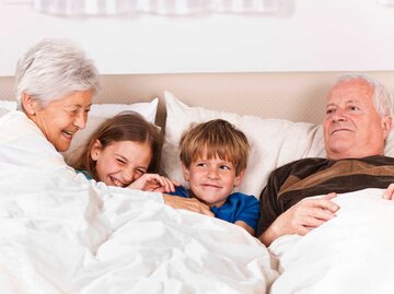 Großeltern liegen mit Enkelkindern im Bett | © Getty Images/vitranc