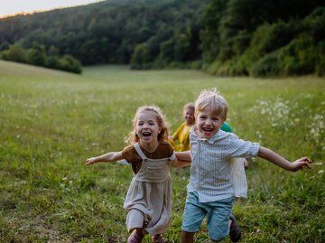 Kinder toben auf einer Wiese | © GettyImages/Halfpoint