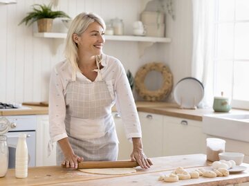 Frau mit Schürze in der Küche und rollt Teig für Plätzchen aus. | © Adobe Stock/fizkes