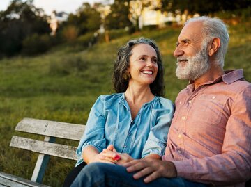 Glückliches älteres Paar sitzt nebeneinander auf einer Parkbank. | © Getty Images / Tim Robberts