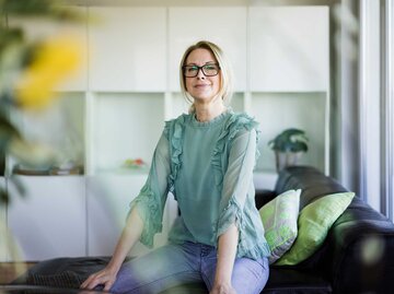 Frau mit Brille sitzt selbstbewusst auf der Couch und trägt eine Brille. | © Getty Images / Westend61