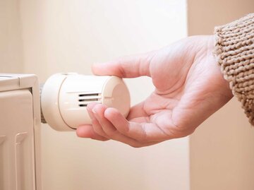 Frauenhand dreht bei der Heizung am Thermostat.  | © Adobe Stock/Özgür Güvenç