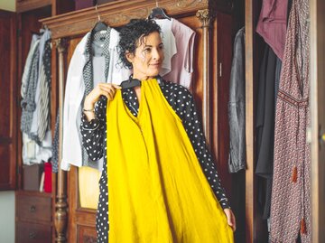 Frau steht vor ihrem Kleiderschrank und hält ein gelbes Kleid hoch | © Getty Images/Eva-Katalin