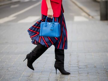 Nahaufnahme einer Frau, die einen rot-blauen Faltenrock trägt, schwarze Stiefel und eine blaue Tasche | © Getty Images/Christian Vierig