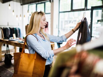 Frau steht im Klamottenladen und begutachtet eine Bluse. | © Getty Images / Tom Werner