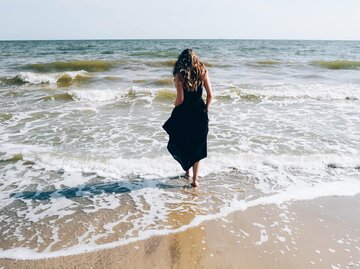 Frau in schwarzem Kleid läuft ins Meer | © Getty Images/Maryna Terletska