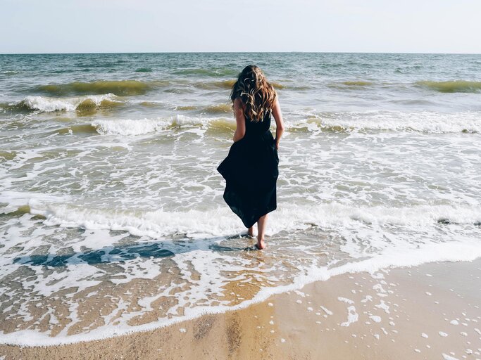 Frau in schwarzem Kleid läuft ins Meer | © Getty Images/Maryna Terletska