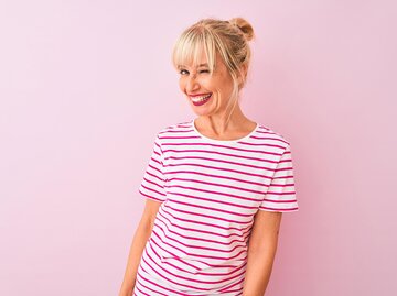 Lachende, blonde Frau in weißem T-Shirt mit pinken Streifen | © Getty Images/AaronAmat