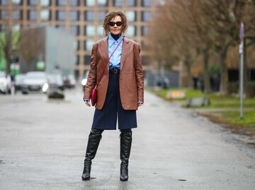Streetstyle von Renia Jaz in braunem Blazer, hellblauem Hemd, navy Shorts und schwarzen Stiefeln | © Getty Images/Edward Berthelot 