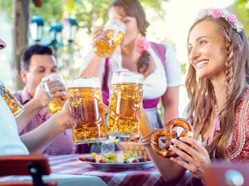 Frau feiert mit Brezel und Bier in der Hand und einem Dirndl auf einem Volksfest | © Getty Images/kzenon