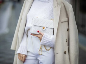 Frau trägt weiße Hose, weißen Pullover, cremefarbenen Mantel und weiße Chanel Tasche | © Getty Images/Christian Vierig