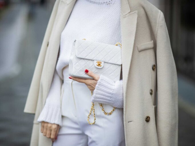 Frau trägt weiße Hose, weißen Pullover, cremefarbenen Mantel und weiße Chanel Tasche | © Getty Images/Christian Vierig