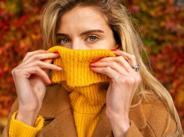 Frau mit blonden Haaren und gelbem Rollkragenpullover vor herbstlicher Kulisse | © AdobeStock/phoenix021