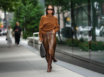 Streetstyle von Aimee Song in einem Strickpullover, Lederrock und Stiefeln in Braun | © Getty Images/Edward Berthelot 