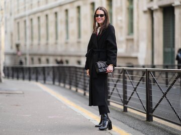 Streetstyle von Frau in einem schwarzen Mantel mit Bindegürtel | © Getty Images/Edward Berthelot