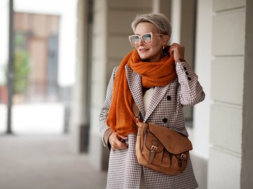 Frau mit Brille trägt herbstlichen Mantel und orangen Schal | © GettyImages/AnnaZhuk