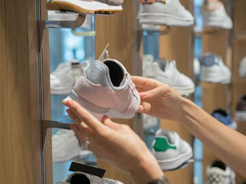 Frau betrachtet in einem Schuhgeschäft einen Sneaker | © Getty Images/mgstudyo