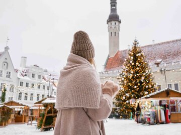 Frau hält eine Tasse in der Hand und blickt auf einen Weihnachtsmarkt | © Getty Images/Iuliia Pilipeichenko
