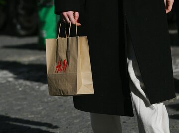 Frau in schwarzem Mantel und weißer Hose hält braune H&M-Tüte in der Hand | © Getty Images/Zed Jameson/Bloomberg 