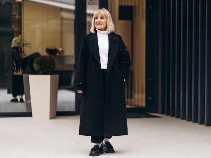 Blonde Frau in schwarzem Mantel, weißem Rollkragenpullover, schwarzer Hose und schwarzen Loafern | © AdobeStock/Petro
