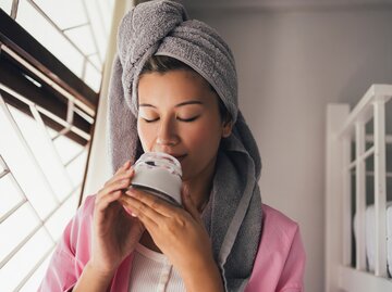 Eine Frau riecht an einem Glas voll Kokosöl und hat ein Handtuch auf dem Kopf | © GettyImages/FreshSplash