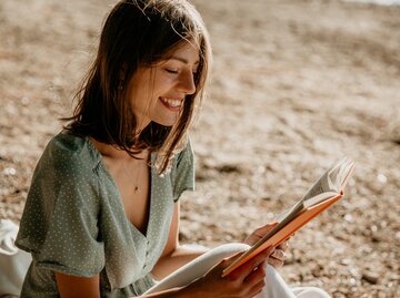 Frau in sommerlichem Kleid liest ein Buch | © GettyImages/Studio4