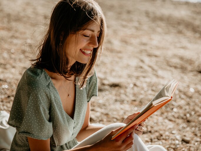 Frau in sommerlichem Kleid liest ein Buch | © GettyImages/Studio4