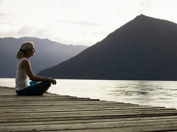 Frau sitzt entspannt auf einem Steg und schaut auf einen See. | © Thomas Barwick, Getty Images